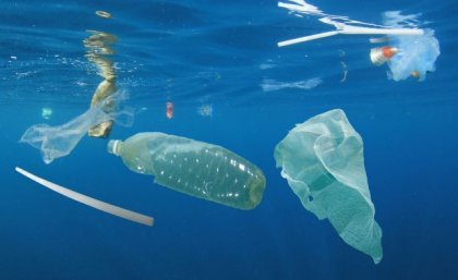 a bottle, plastic bag and straw float in blue water